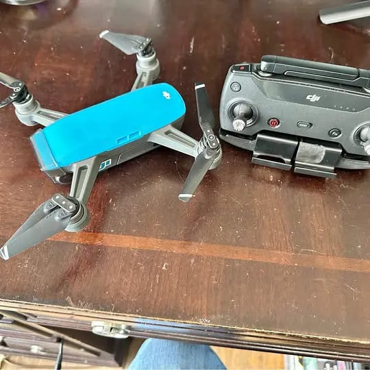 DJI Spark drone with blue body and gray arms, propellers attached, beside remote controller