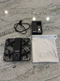 Pocket drone with black frame, controller module, and white drawstring storage pouch