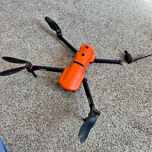 Orange quadcopter drone with four propeller arms and black blades