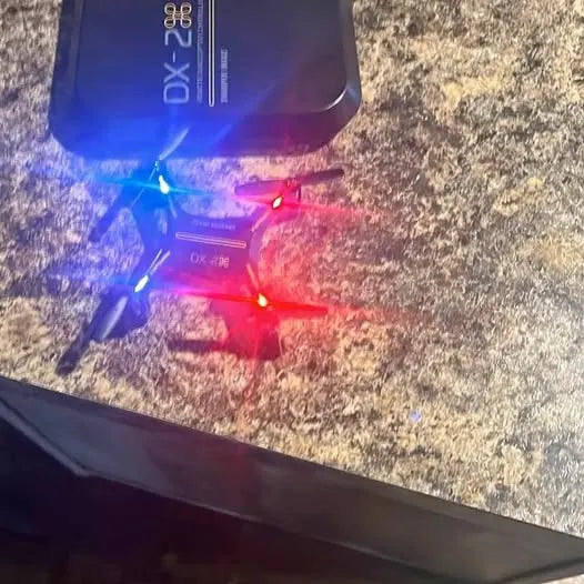 Quadcopter drone with front lights lit, resting on outdoor ground