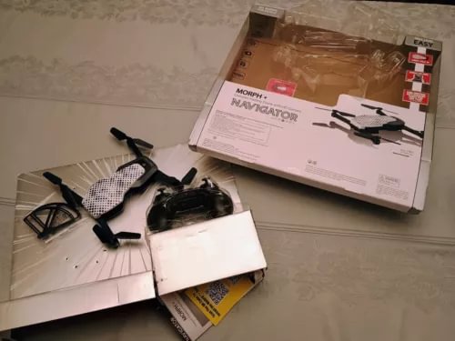 Foldable quadcopter drone with attached camera, beside shipping box and controller parts