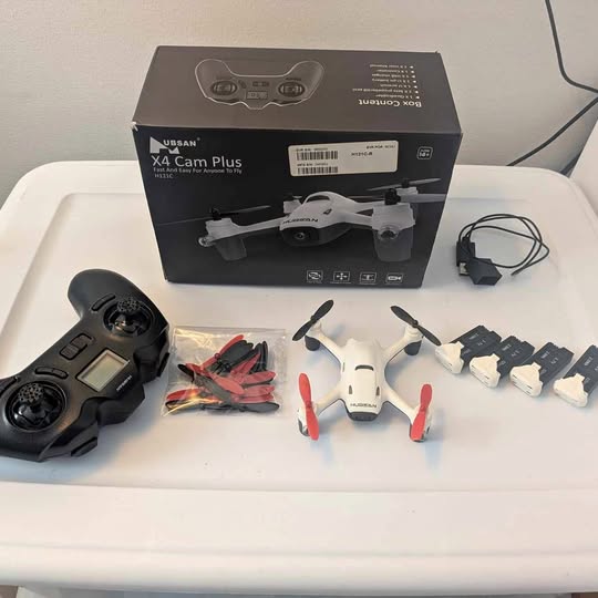 White quadcopter drone kit with black controller, spare propellers, and charger