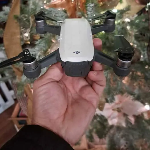 DJI quadcopter drone, white body with four black propellers, held in hand