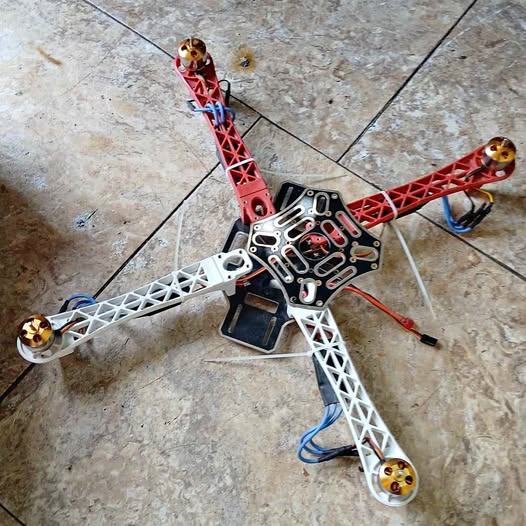 Red quadcopter drone frame with circuit board, wiring and four prop arms
