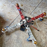 Red quadcopter drone frame with circuit board, wiring and four prop arms