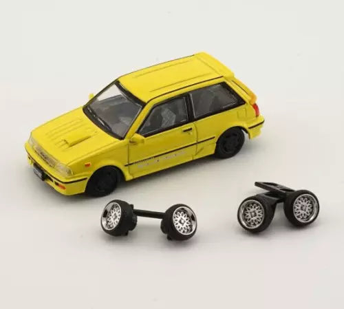 Yellow 1:64 diecast car with black wheels and two sets of spare rims