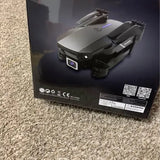Black drone projector shown on retail box, with front lens and foldable arms