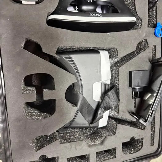 White and black quadcopter drone in protective foam insert, with propellers nearby.