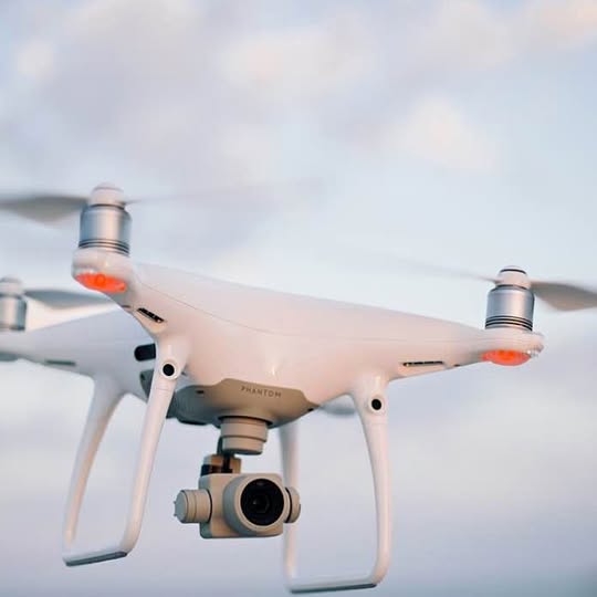 White quadcopter drone with mounted camera and four propellers
