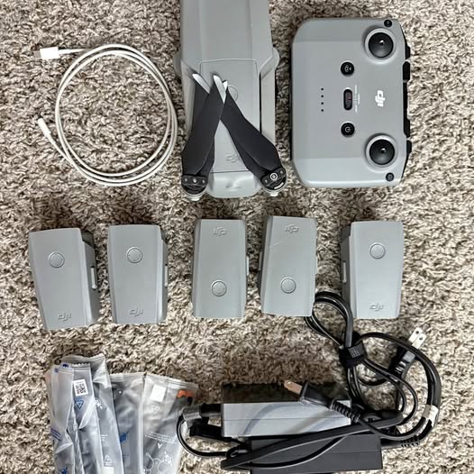 Silver gray drone with camera and multiple batteries, cables, and charging adapter