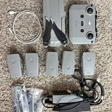 Silver gray drone with camera and multiple batteries, cables, and charging adapter