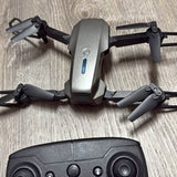 Foldable quadcopter drone with camera mount, gray body and four black propellers.