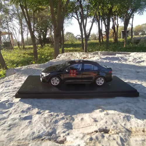 Black diecast model car on dark base, side view with silver wheels and windows