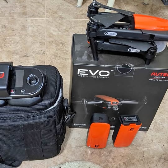 Drone kit with black drone on box, orange remote and two orange batteries, black case.