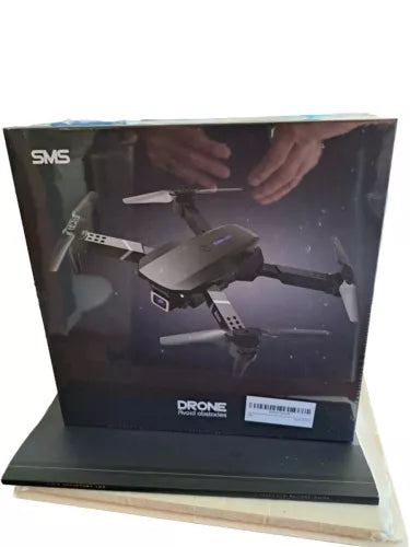 Foldable quadcopter drone shown in retail box, gray with front camera housing
