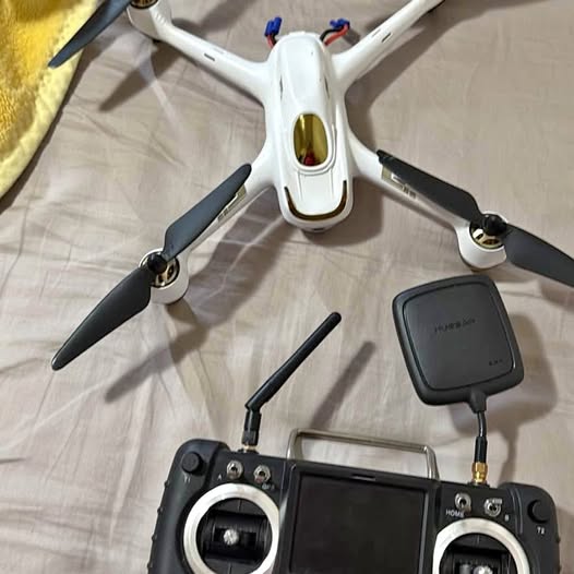 White quadcopter drone with propellers, front camera, and black remote