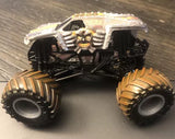 Diecast monster truck with white graphic body and large black wheels, gold accents