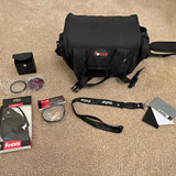 Black camera bag with shoulder strap, lens accessories, and small parts kit