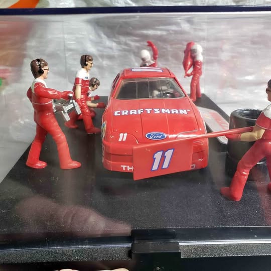 Red diecast race car with number 11 and four red-clad figurines in diorama