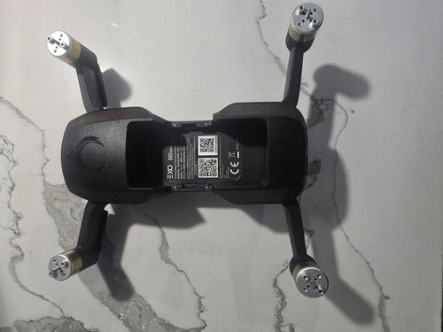 Black quadcopter drone body with arms and underside label panel, no camera attached