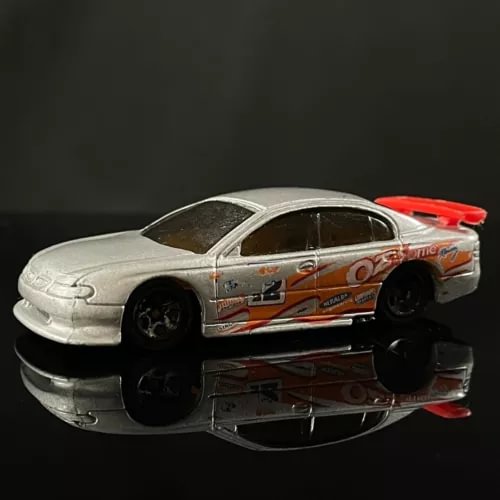 Silver diecast toy car with orange and black racing graphics, 1:64 scale, side view