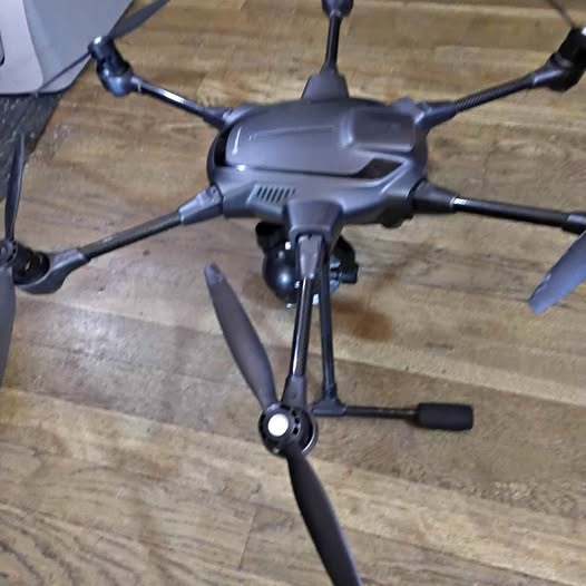 Quadcopter drone with four propeller arms and central camera body, dark gray