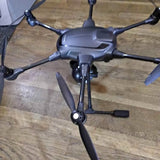 Quadcopter drone with four propeller arms and central camera body, dark gray