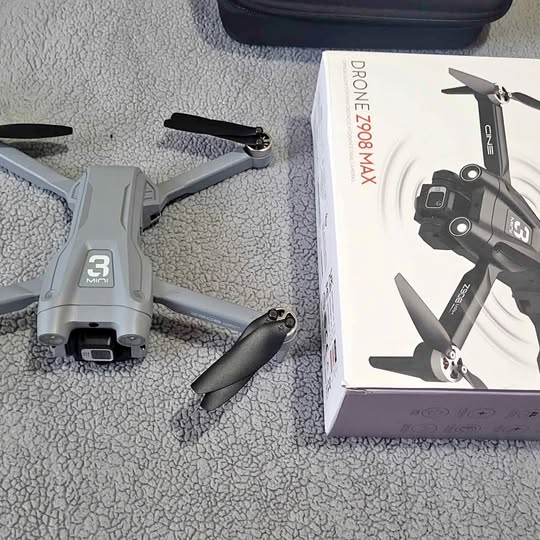 Foldable gray quadcopter drone with 3 mini prop guards, beside product box