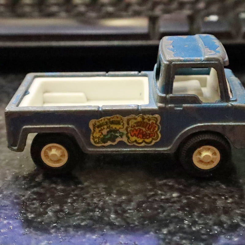 Vintage diecast pickup truck, dark gray with blue cab and worn side decals