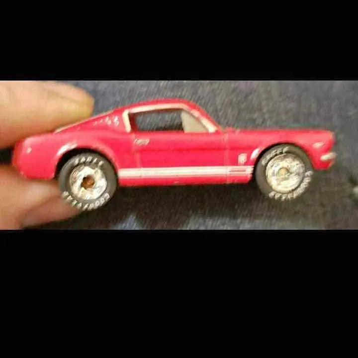 Red diecast toy coupe car with white racing stripe and detailed wheels, side view