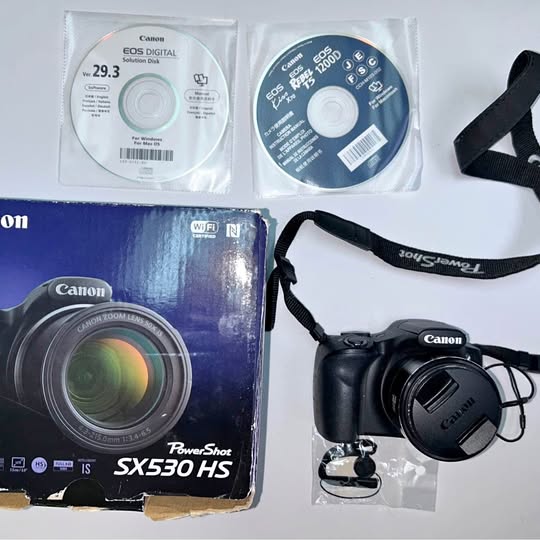 Canon PowerShot SX530 HS digital camera with lens, strap, and accessory discs
