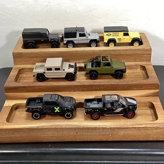 Diecast toy vehicles on wooden tray: black, white, green, yellow trucks and cars