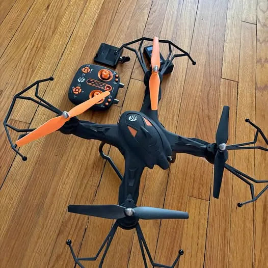 Black quadcopter drone with orange propellers and four arms, viewed top down.