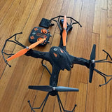 Black quadcopter drone with orange propellers and four arms, viewed top down.