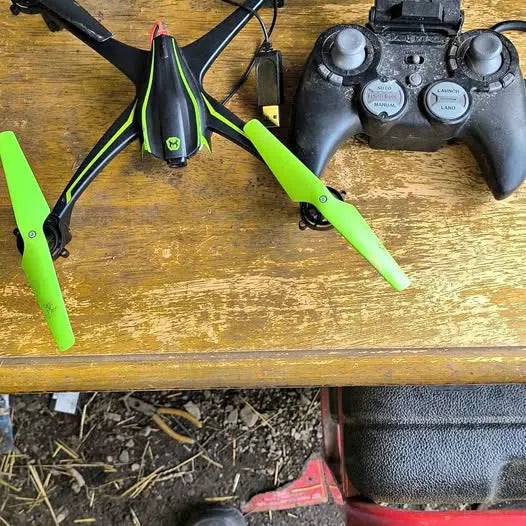 Green and black quadcopter drone with four propellers, shown on a tabletop.