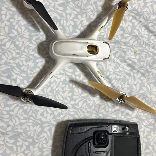 White quadcopter drone with front camera and gold propellers, viewed from above