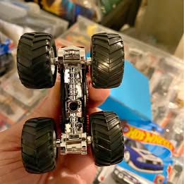 Diecast monster truck with four dark knobby wheels and chrome chassis, underside view