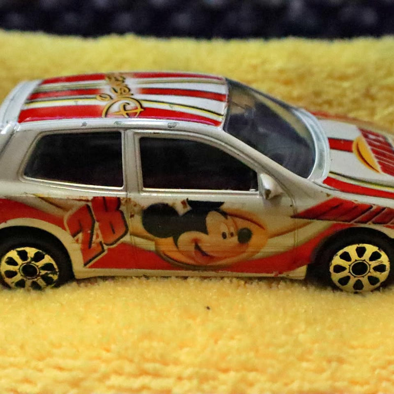 Die-cast model car with Mickey Mouse decals, beige body, red racing stripes, 1/43 scale.