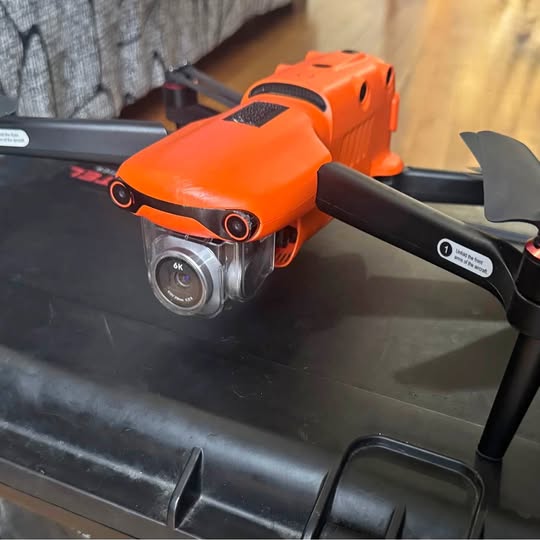 Orange foldable drone with 6K camera, resting on black case