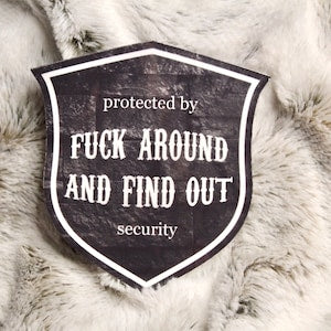 Black shield patch with white text: protected by FUCK AROUND AND FIND OUT security