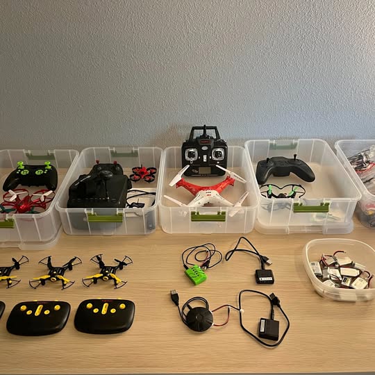 Set of seven quadcopter drones with remotes and parts in plastic storage bins