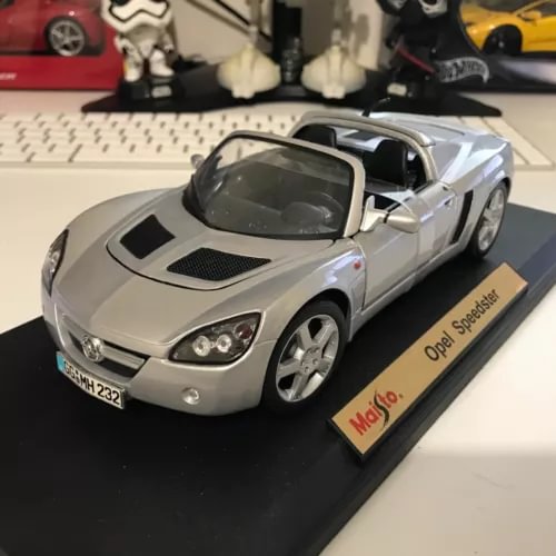 Silver diecast model car with black hood insets and dark windows on display base