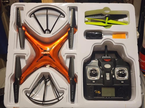 Syma RC quadcopter drone with orange body and black 2.4G remote controller, shown in box
