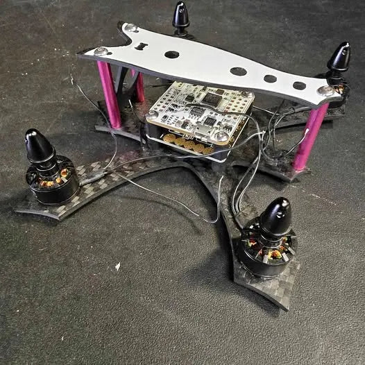 Small quadcopter drone with pink arms and exposed circuit boards