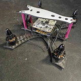 Small quadcopter drone with pink arms and exposed circuit boards