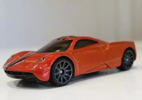Orange 1:64 scale diecast toy car with black hood and racing decals