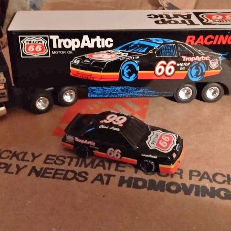 Diecast NASCAR trailer truck with race car, black and orange, blue wheels