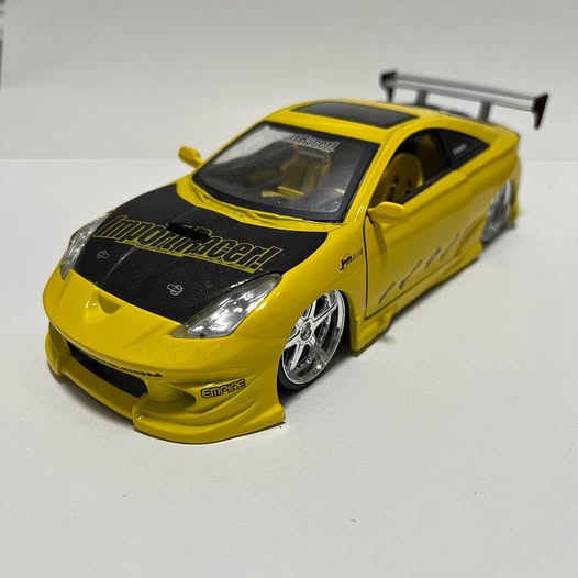 Yellow Toyota Celica diecast racer, front 3/4 view with black hood stripe and hood vents