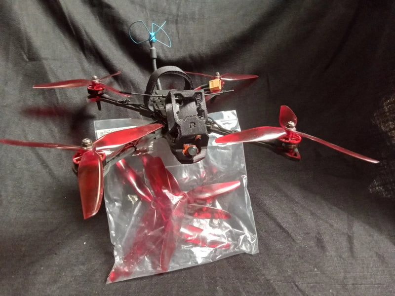 Racing quadcopter drone with red propellers, black frame, and mounted camera module