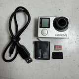 Silver action camera with touchscreen, lens, battery, USB cable, and microSD card